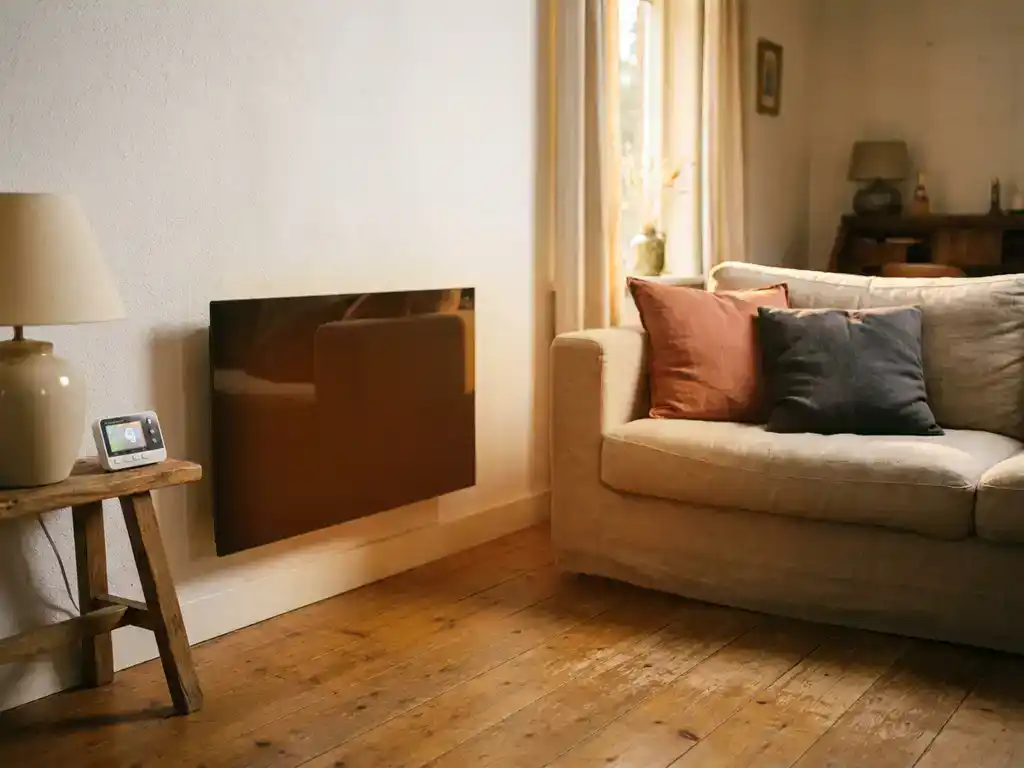 Infrarood verwarmingspaneel aan witte woonkamermuur met houten vloer, linnen bank en energiemeter op bijzettafel.