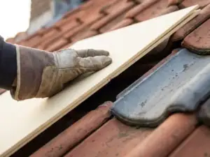 Dakdekker installeert dunne stijve isolatieplaat op terracotta dakpannen van Nederlandse woning.