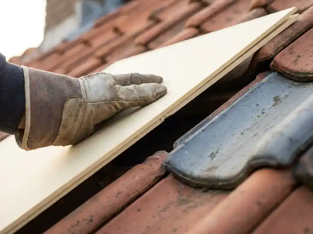 Dakdekker installeert dunne stijve isolatieplaat op terracotta dakpannen van Nederlandse woning.