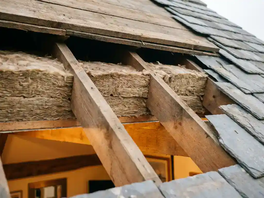 Dwarsdoorsnede van dakisolatiepanelen tegen houten dakspanten, met luchtspouw en warm interieurlicht zichtbaar.
