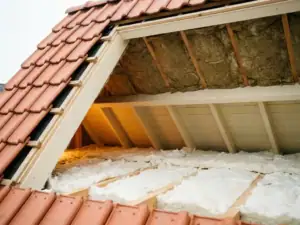 Dakdoorsnede van Nederlandse woning met mineraalwol tussen dakspanten en isolatiedeken op zoldervloer, terracotta dakpannen zichtbaar.