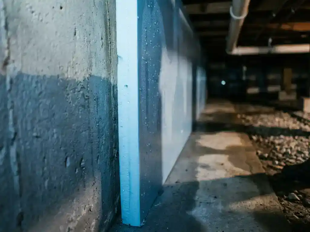 XPS isolatieplaat tegen vochtige betonnen funderingsmuur in kruipruimte, waterdruppels zichtbaar op het oppervlak.