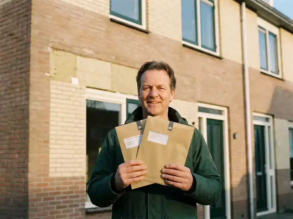 Huiseigenaar houdt twee subsidie-enveloppen vast voor een recent geïsoleerde Nederlandse woning in warm middaglicht.