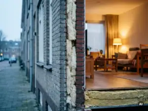 Doorsnede van Nederlandse rijtjeswoning met dikke isolatielagen in spouwmuren en houten vloer, warm interieur contrasteert met grijze baksteen.